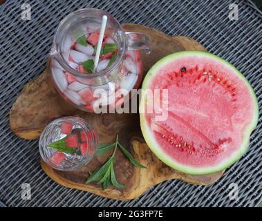 decanter di acqua ghiacciata con cubetti di melone d'acqua e foglie di menta, vetro riempito e mezzo melone d'acqua sul lato Foto Stock