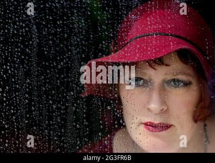 Donna che guarda attraverso la finestra coperta di gocce di pioggia. Foto Stock