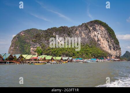 Spettacolari formazioni rocciose e scogliere con un villaggio d'acqua costruito su palafitte, a Phang Nga Bay Thailandia Foto Stock