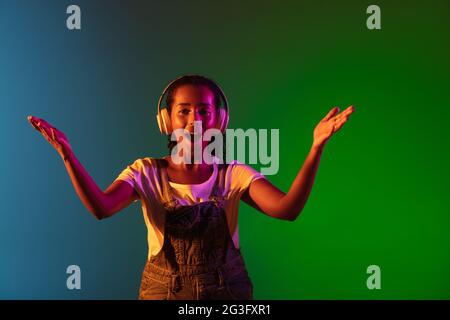 Latino cantante ritratto femminile isolato su sfondo studio in luce al neon. Bella modello femminile in nero con microfono. Foto Stock