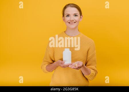 Attraente donna casalinga tiene tubo con vitamine in mano e dare pillole a qualcuno set, sorridente avendo buon umore guarda la fotocamera trattamento e. Foto Stock