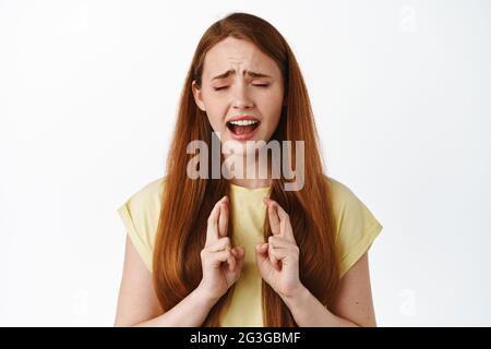 Disperato e speranzoso studente di bambina rossa che prega, facendo desiderio con le dita incrociate, sobbando e implorando dio, soppiantando per qualcosa accadere Foto Stock