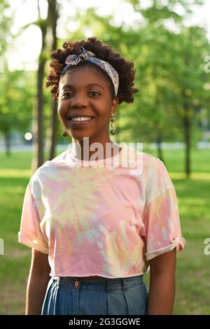 Ritratto di giovane donna africana che sorride alla macchina fotografica mentre si trova nel parco Foto Stock