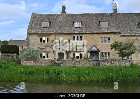 Una fila di case si trova vicino al River Eye che scorre attraverso il pittoresco villaggio di Lower Slaughter, una popolare destinazione turistica in questa parte o Foto Stock