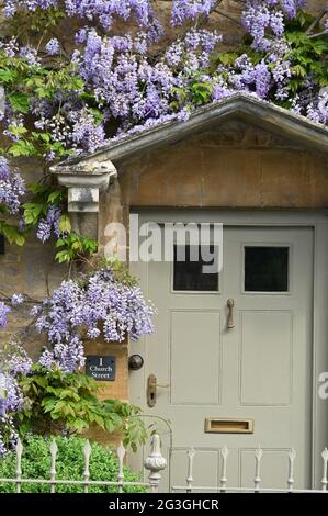 Glicine in fiore intorno alla porta di una proprietà in Church Street nel nord Oxfordshire villaggio di Kingham Foto Stock