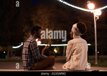 Giovane coppia seduta sulla panchina la sera nel parco e che parla l'un l'altro Foto Stock