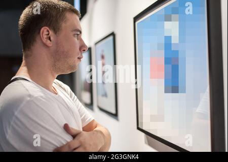 Giovane uomo in galleria d'arte moderna che contempla opere d'arte. Pittura astratta Foto Stock