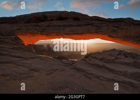 Luce magica dalla prima luce riflessiva sul Mesa Arch che si affaccia sulle guglie gemelle del Woman Arch e della Monster Tower nella Canyonlands Natia dello Utah Foto Stock