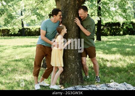 Una coppia di maschi gay che gioca con la loro figlia adottiva all'aperto nel parco Foto Stock