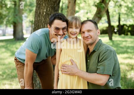 Ritratto di felice coppia gay maschio con bambino sorridente a macchina fotografica mentre si cammina nel parco Foto Stock