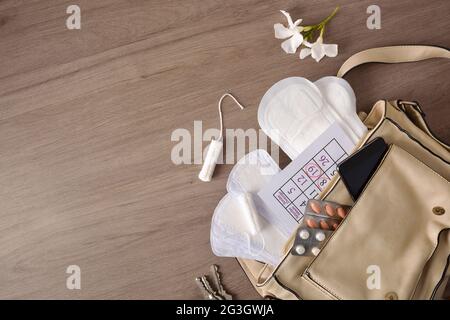 Borsetta con vari prodotti per l'igiene mestruale e protezione covid-19 per le donne su tavolo di legno. Vista dall'alto. Foto Stock