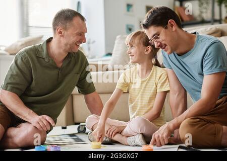 Famiglia gay seduta sul pavimento con la loro figlia adottiva e passare il tempo insieme in camera Foto Stock