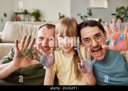 Ritratto di felice famiglia gay con bambino mostrando le loro mani dipinte e sorridendo alla macchina fotografica Foto Stock