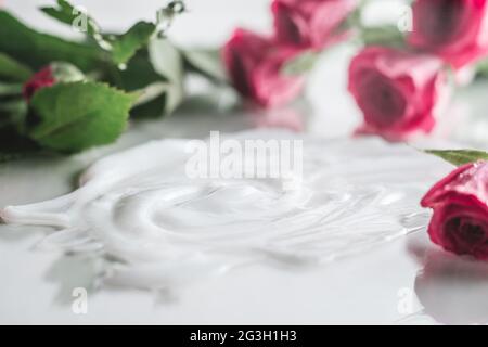 Crema bianca cosparsa su superficie lucida circondata da rose rosa delicate e sfocate Foto Stock