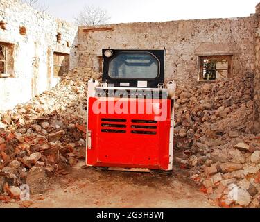 Una minipala caricatrice a fuselli in un'azienda agricola italiana parzialmente demolita in pietra vecchia in provincia di Udine, Friuli-Venezia Giulia, NE Italia Foto Stock