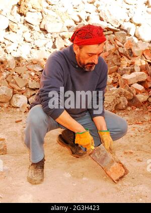 Un uomo raschia il cemento in eccesso da mattoni antichi che vengono recuperati per ulteriore uso architettonico dal sito di demolizione di un vecchio edificio agricolo italiano. Foto Stock