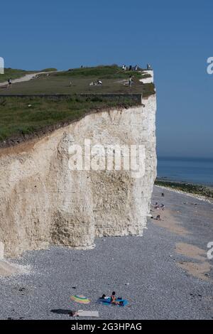 I bagnanti del sole hanno scelto probabilmente il posto più pericoloso per prendere il sole mentre hanno impregnato sul sole d'estate a destra sotto il bordo della scogliera a Beachy Head, Foto Stock