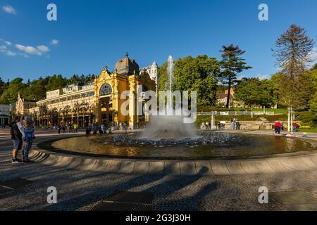 Marianske Lazne, Repubblica Ceca - Maggio 30 2021: Vista della fontana d'acqua che si sprona. Edificio giallo colonnato sullo sfondo. Giorno di primavera soleggiato. Foto Stock