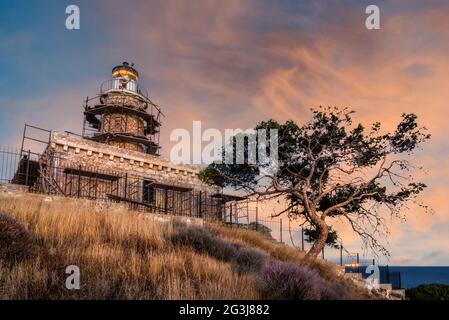 Isola di Salamis, Grecia. Il faro costruito in pietra a capo Koghi nell'isola di Salamis al tramonto con il cielo nuvoloso colorato Foto Stock