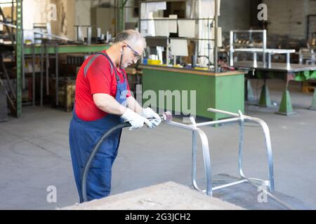Il collarino blu che lucidano un pezzo di metallo in un impianto di produzione. Lucidatrice impegnata e concentrata mentre si lavora in una fabbrica. Foto Stock