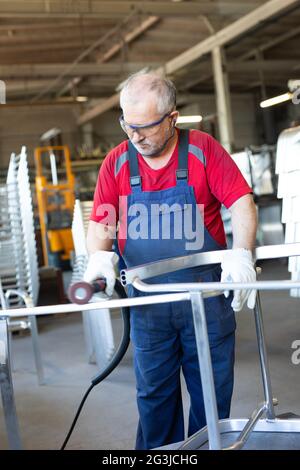 Il collarino blu che lucidano un pezzo di metallo in un impianto di produzione. Lucidatrice artigiano occupato e concentrato mentre si lavora in una fabbrica. Foto Stock