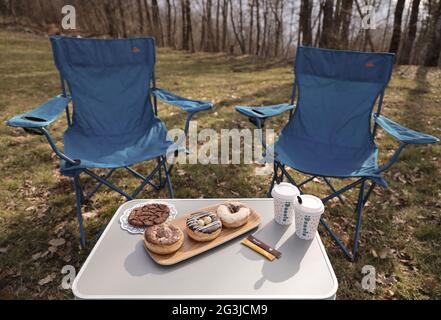 Tavolino con ciambelle, due tazze di caffè su di esso e due sedie in un parco Foto Stock