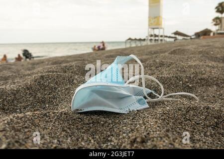 Maschera chirurgica blu lasciata dietro su una spiaggia, Spagna. Foto Stock