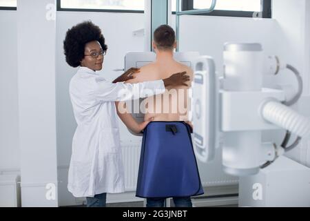 Giovane donna africana dottoressa radiologa, o tecnico radiologico, che esegue la scansione radiografica del torace di un giovane paziente maschile in una moderna sala esame Foto Stock