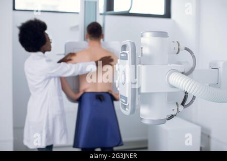 Giovane donna africana dottoressa radiologa, o tecnico radiologico, che esegue la scansione radiografica del torace di un giovane paziente maschile in una moderna sala esame Foto Stock