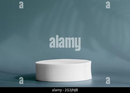 Palco circolare per prodotti cosmetici con ombra di piante tropicali sulla parete. Piedistallo rotondo per la presentazione del packaging su sfondo blu con Foto Stock
