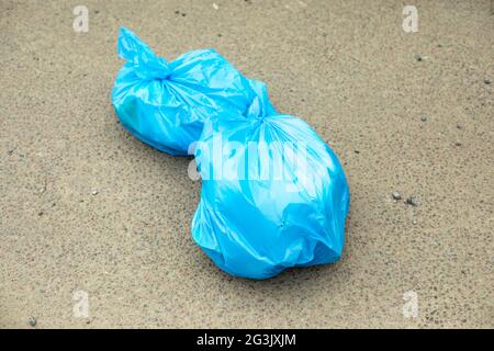 Sacco per rifiuti sulla strada. Un sacchetto blu di spazzatura si trova sull'asfalto. I rifiuti domestici vengono gettati nel posto sbagliato. Foto Stock