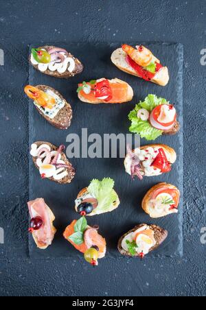 Set di panini di tapas di pesce spagnolo - gamberi, polpo, calamari, salmone, formaggio gorgonzola, crema di formaggio, erbe, uva e olive verdi con bluebe Foto Stock
