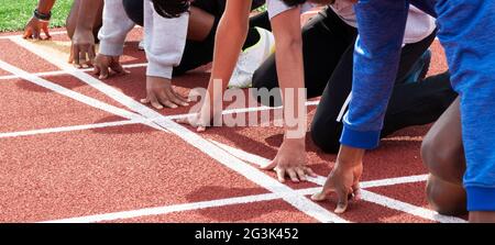 Cinque ragazzi delle scuole superiori sul loro segno alla linea di partenza pronti a sprint l'uno contro l'altro nella pratica in pista. Foto Stock