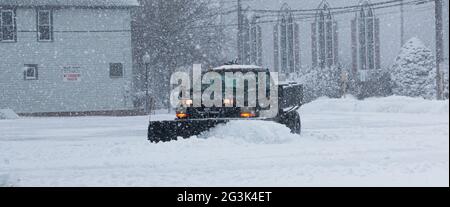 Camion nero con un aratro da neve che si stagliano un parcheggio dietro le aziende mentre la neve sta ancora cadendo duro durante una bizzarda. Foto Stock