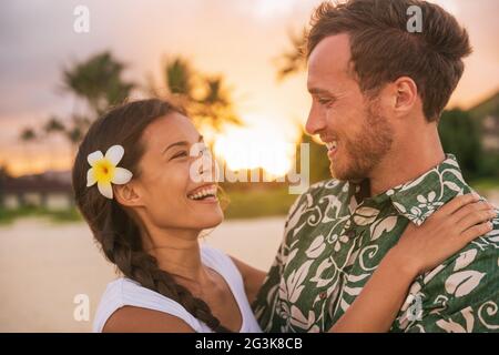 Felice coppia amanti in amore sulla romantica vacanza al tramonto spiaggia in Hawaii viaggio. Donna asiatica abbracciando uomo caucasico sorridente, rapporto interrazziale Foto Stock