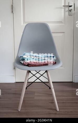Pila di vestiti puliti ripiegati su una moderna sedia davanti alla porta. Foto Stock