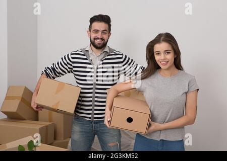 Attraente coppia giovane è in movimento, sorridente e scatole di contenimento mentre in piedi tra spacchettato caselle. Foto Stock