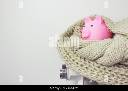 Banca di piggy con soldi e sciarpa sul radiatore. Concetto di stagione di riscaldamento. Foto Stock