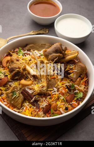 Indiano Mutton biryani preparato in riso Basmati servito con yogurt tuffo su sfondo moody, fuoco selettivo Foto Stock