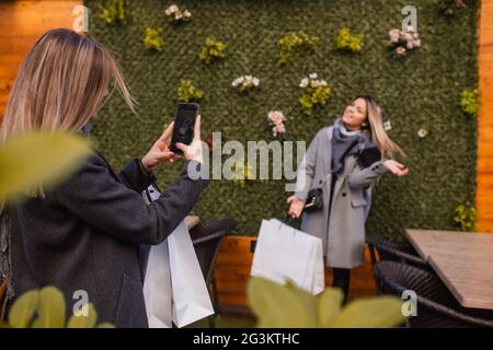 Due bellissimi amici biondi nello shopping in città. Una ragazza scatta una foto di un'altra mentre tiene una borsa in mano e dispone una pettinatura. Foto Stock