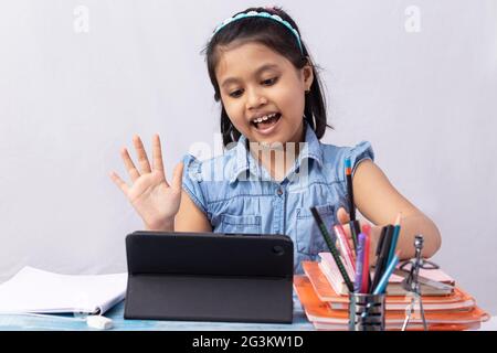 Un bambino indiano grazioso della ragazza che assiste in classe in linea con il tablet su sfondo bianco Foto Stock