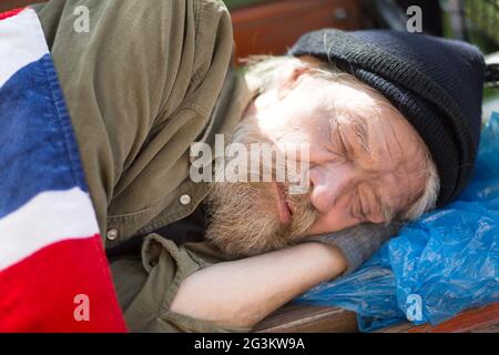 Close up portrait of homeless man sleeping on bench in city park. Stock Photo