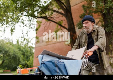 View of homeless man walking pushing shopping cart. Stock Photo