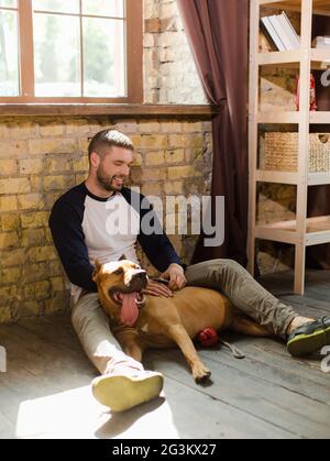 View of young sportive man having fun with dog at home. Stock Photo