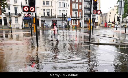 Brighton UK 17 giugno 2021 - UN pedone salta sopra l'acqua alluvionale sulle strade a Valley Gardens a Brighton dopo una notte di pioggia pesante e temporali nel sud-est : Credit Simon Dack / Alamy Live News Foto Stock