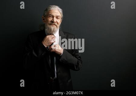 Ritratto di un anziano in tuta nera e camicia bianca. Foto Stock