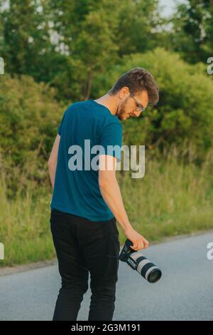 Scatto verticale di un fotografo bosniaco che cammina su una strada rurale vuota con la sua macchina fotografica Foto Stock