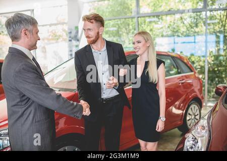 Concessionario di veicoli che passa le chiavi dalla nuova auto alla giovane coppia felice Foto Stock