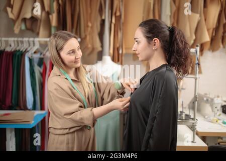 dressaker al lavoro che fa le misure del cliente. Il modello è venuto a provare su un vestito. Dressaker fa la sabbiatura del tessuto Foto Stock