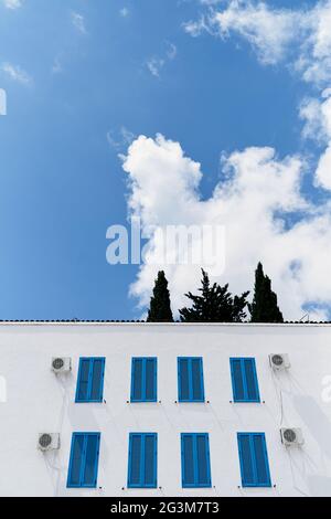 Edificio bianco a due piani con persiane blu chiuse sulle finestre sullo sfondo di cielo blu e nuvole bianche Foto Stock